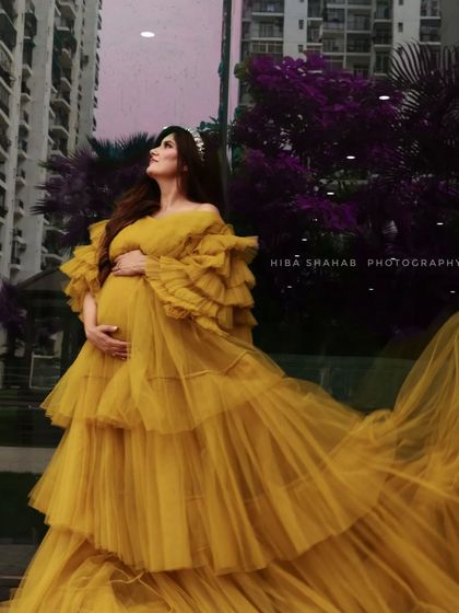 A client looking stunning in a mustard yellow ruffled gown against an urban backdrop. The dramatic sleeves and tiered skirt make this a high-impact choice for your photoshoot.