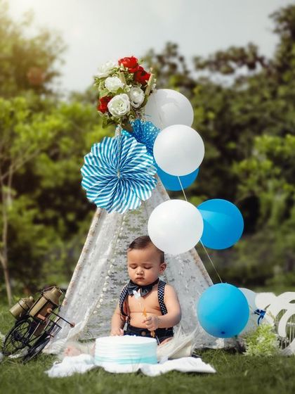 A fun cake smash moment from a blue-themed outdoor first birthday party setup, complete with a teepee and balloons.