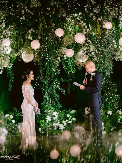 The groom reads his vows to his bride against a stunning backdrop of hanging greenery and glowing orbs, a magical and romantic setting.