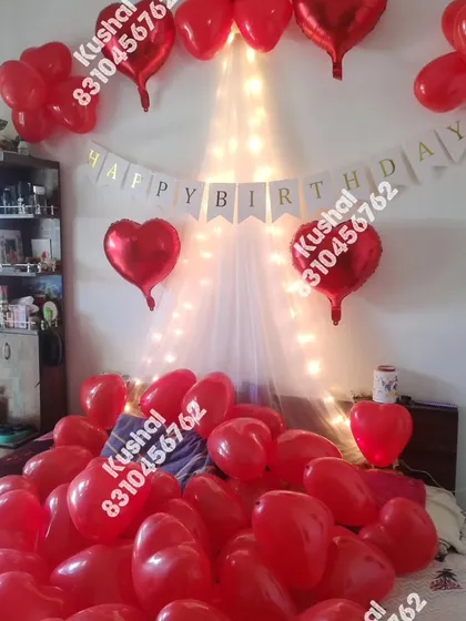 A classic romantic birthday surprise with a bed full of red heart-shaped balloons and a fairy light canopy.