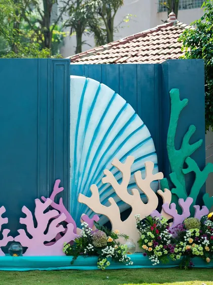 This is a section of the custom-built backdrop for an aqua-themed mehendi party. The design features large seashells and colorful coral cutouts to create an immersive under-the-sea experience for the celebration.