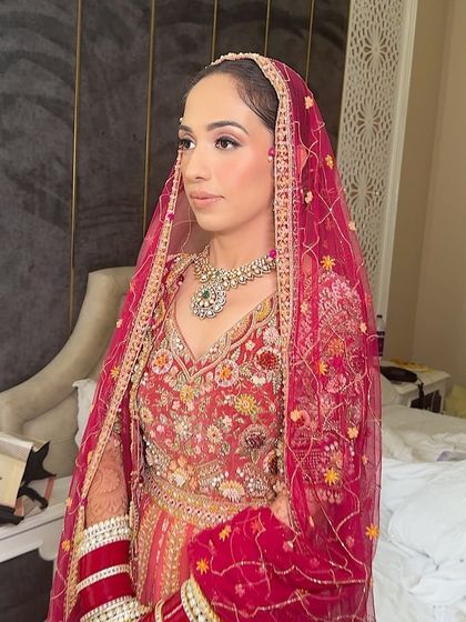 A full view of the bride's beautiful red and pink outfit. The makeup was designed to be soft and elegant to complement the intricate details of her attire.