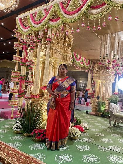 Our client Swetha Babu, looking regal in the classic red and blue Kanchi silk saree against a backdrop of opulent wedding decorations.