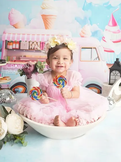 The birthday girl sits in a bowl holding lollipops, surrounded by the sweet Candyland theme. Her happy expression is the centerpiece of this fun milestone photo.