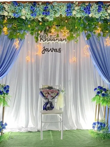 A dreamy backdrop for an evening event, featuring blue and white drapes. The setup is enhanced with a canopy of artificial leaves, fairy lights, and glowing moon and star cutouts for a celestial theme.