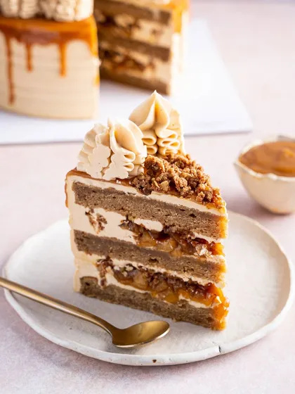 A close-up of a slice of our Apple & Salted Caramel Cake, highlighting the distinct, generous layers. The spiced apple filling and crumble are clearly visible, promising a dessert full of texture and warmth.