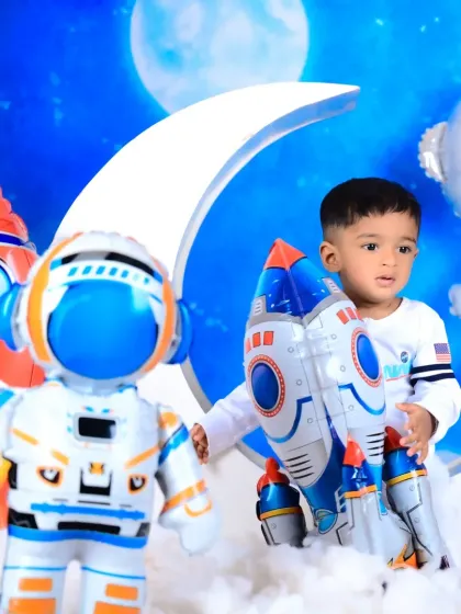 A little astronaut exploring space with rockets and planets. The blue background and moon prop create a celestial atmosphere.