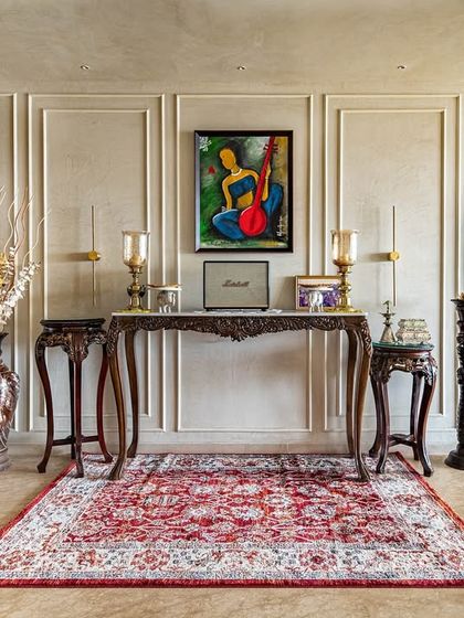 This elegant foyer sets a welcoming tone with its classic wall moulding, traditional carved wood console table, and a vibrant Persian rug. The space blends India-Modern aesthetics with timeless design elements.