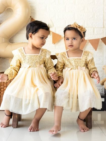 Twin sisters celebrating their second birthday in matching golden dresses. This rustic setup with a '2' balloon and 'TWO' blocks is perfect for a shared milestone.