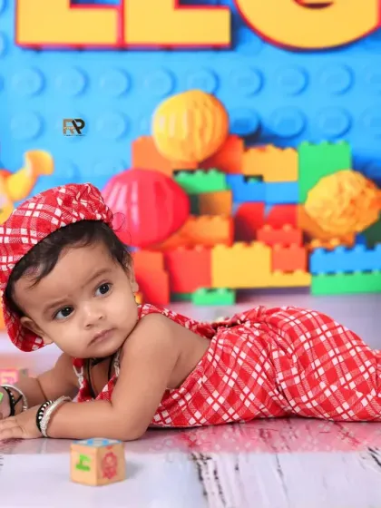 A baby boy in a red checkered outfit plays with blocks in a colorful Lego-themed setup. The bright colors and familiar toys make this a fun and engaging shoot for little builders.