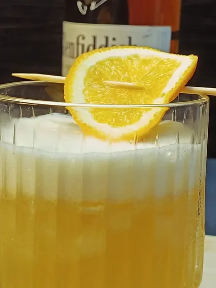 A close-up of the Whisky Sour, garnished with a simple orange slice. The key is in the shake, which creates the signature foam from the egg white.