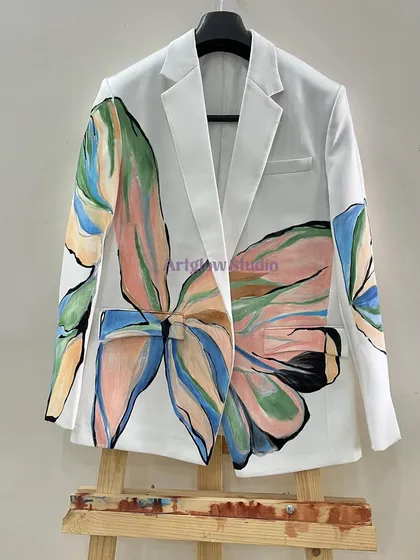 This white blazer features a large, abstract floral design in a soft pastel palette. The artwork flows across the front and onto the sleeves, creating a bold yet elegant statement piece.