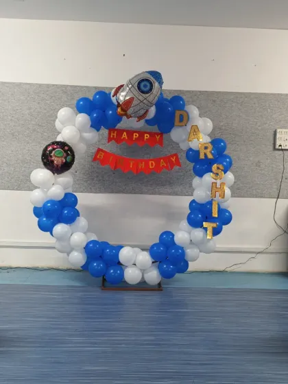 An out-of-this-world Astronaut theme birthday decoration. This setup includes a circular balloon backdrop in blue and white, rocket and astronaut foil balloons, and personalized name lettering.