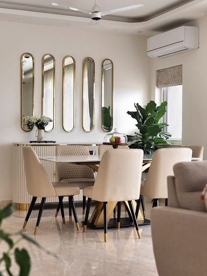 This dining space exudes modern glamour. A set of five elongated oval mirrors with gold frames creates a stunning feature wall, making the room feel larger and brighter. The plush beige chairs and sleek table complete the luxurious look.