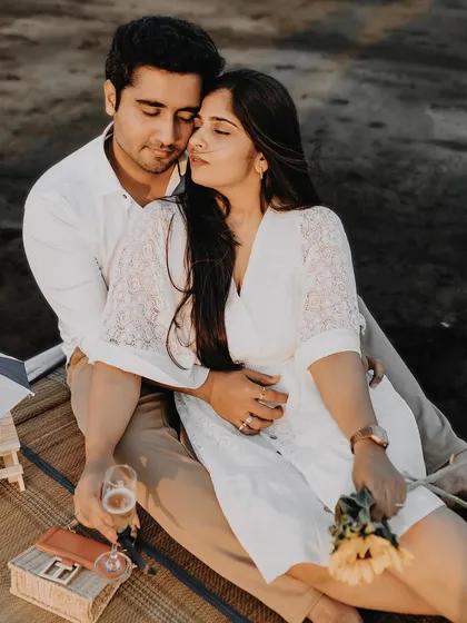 A cozy and romantic beach picnic setup. The couple shares an intimate moment, enjoying a glass of champagne as the sun sets, creating a perfect scene for a relaxed pre-wedding shoot.