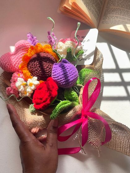 A stunning, colorful "Lover's Bouquet" held in hand. This arrangement features a mix of a sunflower, tulip, rose, and a crochet heart, making it the ultimate romantic gesture.