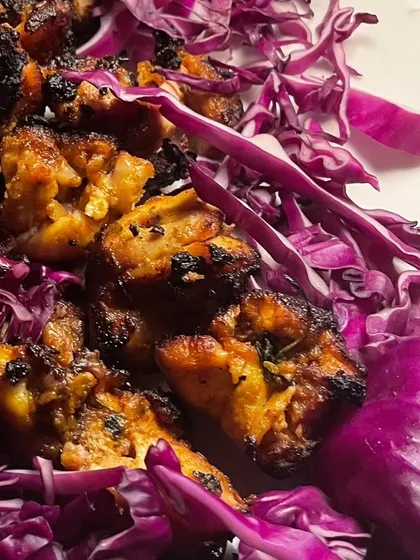 Grilled chicken pieces served on a bed of purple cabbage. This simple yet flavorful dish is a great option for a healthy and delicious catering spread.