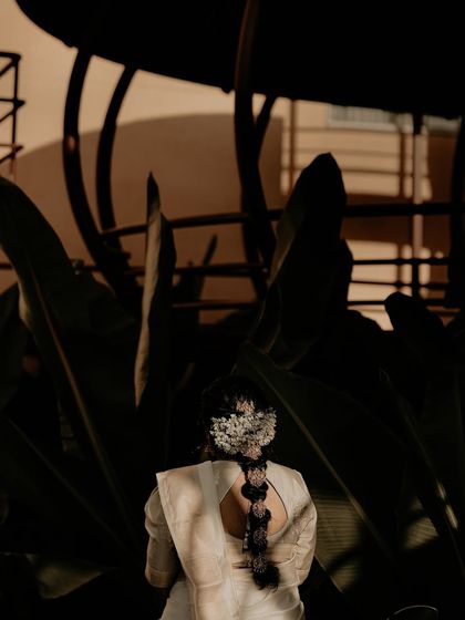 A beautiful shot focusing on the back details of the bride's look. The traditional gajra in her hair stands out against the dark, moody background of tropical plants.
