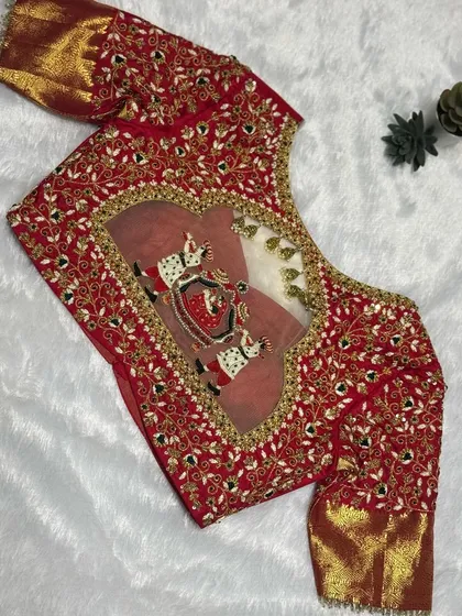 A classic bridal look that never fails. This fiery red blouse features a detailed palanquin (doli) scene embroidered within a heart-shaped back cutout, framed by intricate floral zardosi work. This is storytelling through thread.