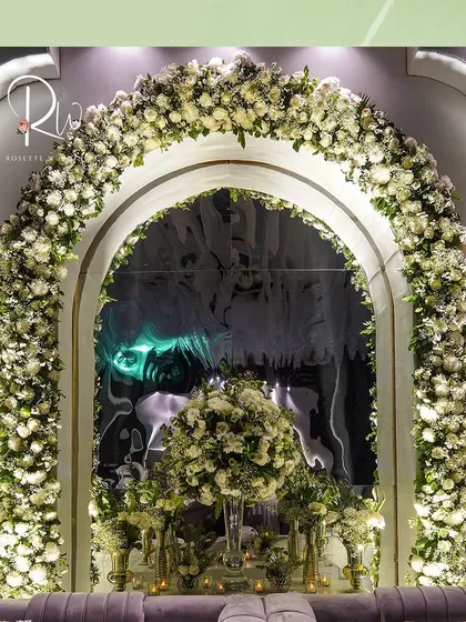 A photo booth area for an enchanted forest-themed event, featuring a large arch of white roses and a plush grey sofa.