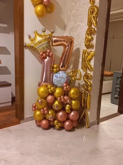 A compact balloon bouquet for a 17th birthday. It features rose gold and gold balloons, a crown foil, and the name 'RAKSHI' spelled vertically.