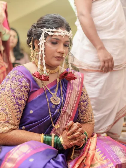 A beautiful textured bun hairstyle for a Marathi bride, perfectly complementing her purple Nauvari saree and traditional Mundavalya for the ceremony.