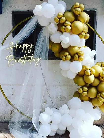 A simple and chic outdoor balloon ring. The white and gold balloons are elegantly draped over a gold hoop, with a sheer white cloth for a soft, dreamy effect.