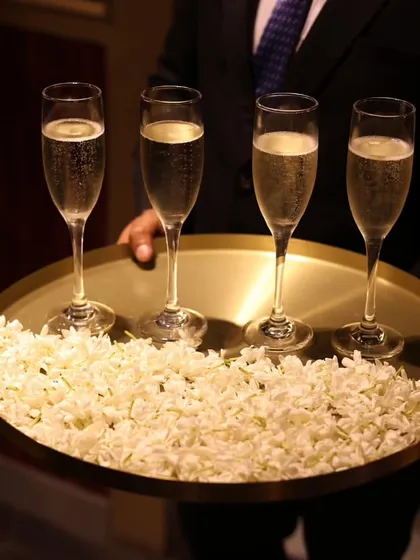 A touch of elegance in our beverage service. A server presents a tray of champagne flutes resting on a bed of fresh jasmine flowers, adding a fragrant and beautiful detail to the experience.