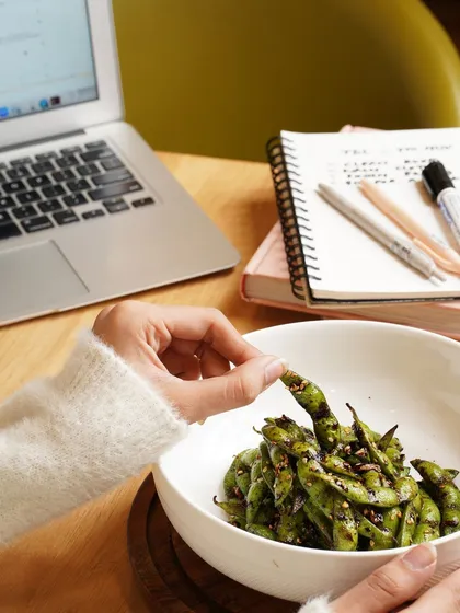 A relatable shot of someone snacking on healthy edamame while working, positioning the cafe as a great spot for a working lunch.