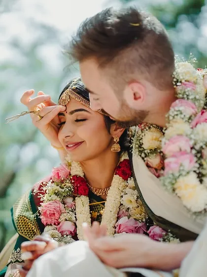 A gentle, intimate moment. The groom-to-be helps with the bride's bindi, a beautiful detail captured in the soft light of our gardens.