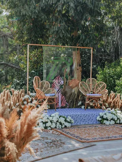 A wider view of the jungle-themed jaimala stage. Set against a backdrop of lush trees, the cane chairs and tiger print create a bold and unforgettable setting for the couple.