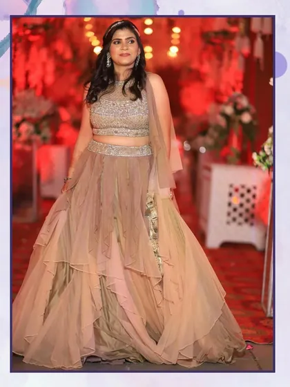 This client is glowing in a layered net lehenga in a subtle beige tone. The tiered skirt adds beautiful volume and movement, making it ideal for a reception party.