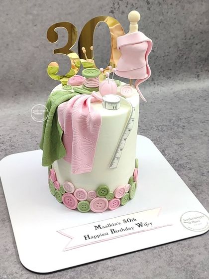 A chic cake for a fashion designer's 30th birthday. The cake is adorned with edible fabric, a measuring tape, buttons, and a miniature mannequin.