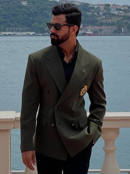 An olive green double-breasted blazer with a unique gold crest, styled for a refined look against a stunning seaside backdrop. This is a perfect example of a versatile travel blazer.
