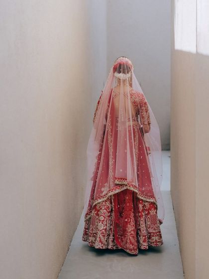 A unique perspective of the bride walking down a narrow hallway, her red lehenga filling the frame. This shot is about mystery and anticipation, a glimpse of the bride before her grand reveal.