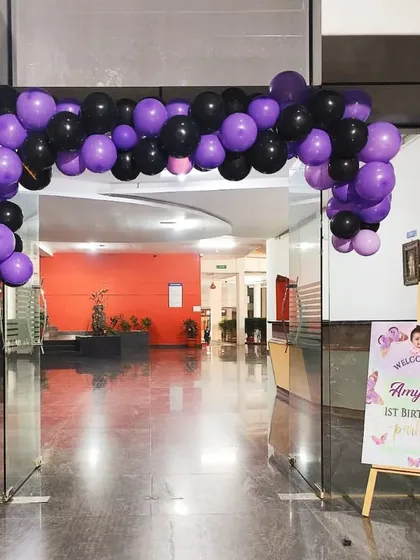 A purple and black balloon arch at the entrance of a large hall, setting the theme for the party inside.
