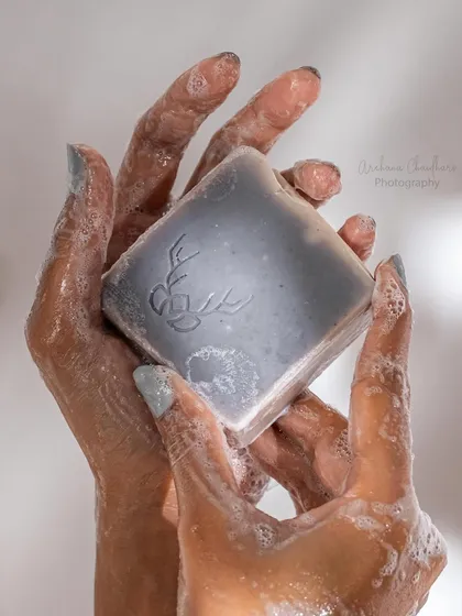 Another angle of a hand model holding a wet bar of soap. The focus here is on the rich lather and the product's embossed logo, highlighting its quality and branding.