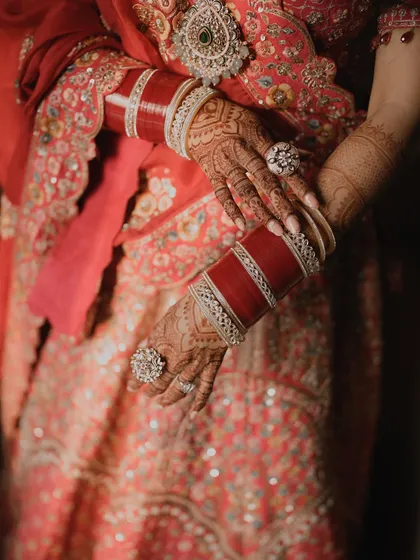 A close-up of the bride's hands, showcasing her beautiful red chooda bangles and intricate mehndi.