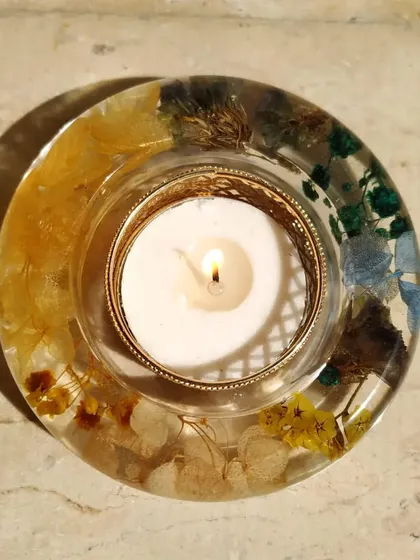 This round resin diya features a mix of colorful preserved flowers, creating a beautiful, natural look. The lit candle in the center casts a warm glow, highlighting the delicate petals within the resin.