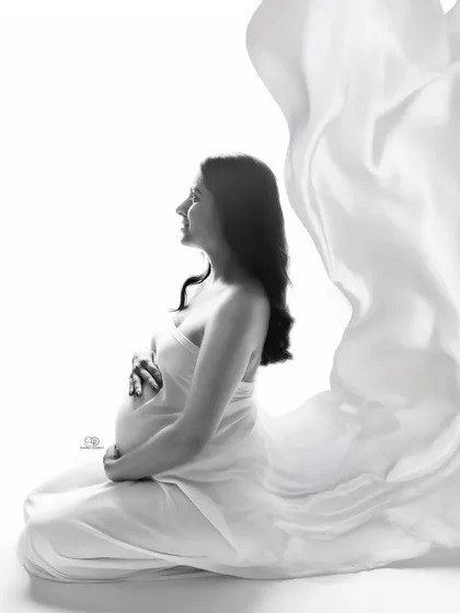 The pure and simple beauty of expecting, captured in a classic black and white portrait. The flowing white fabric creates a soft, ethereal feel, focusing on the beautiful silhouette of the baby bump.