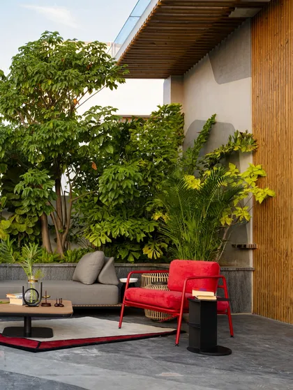A terrace transformed into an urban sanctuary. This rooftop garden uses a dense backdrop of trees and a bold red accent chair to create a private escape with a strong visual identity against the city skyline.