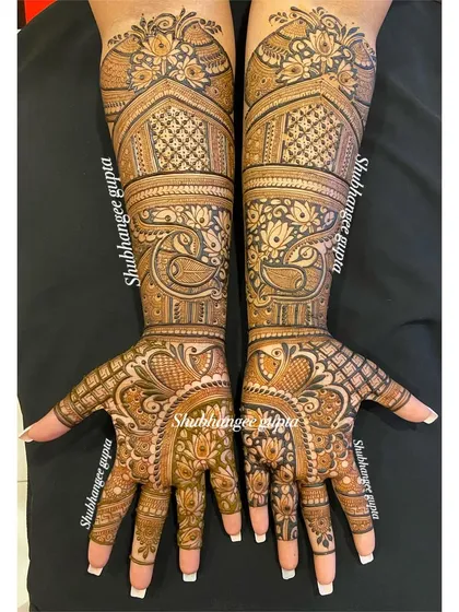 An elegant bridal design where the patterns on each hand are different but complementary. One palm features a peacock and the other a lotus, tied together with similar architectural motifs on the arms.