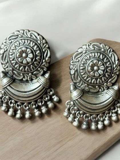 Elegant and stunning silver oxidised earrings. This pair features a large, circular stud with a dangling half-moon element and ghungroos.