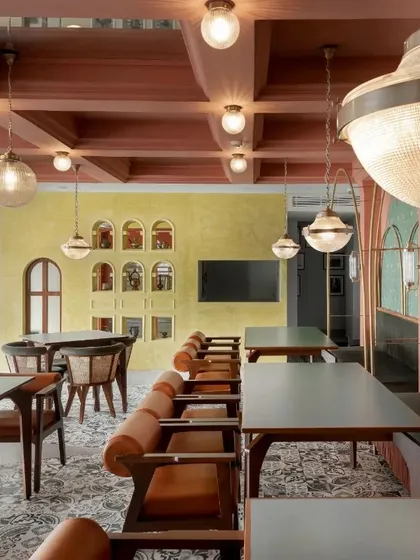 A view across the restaurant showing the interplay of different zones. A wall of arched niches in a contrasting yellow-green stucco finish serves as a vibrant backdrop.