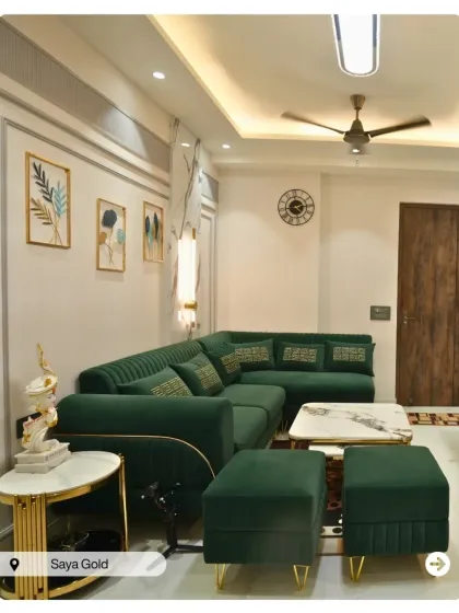 An emerald green L-shaped sofa brings a sense of luxury to this living room at Saya Gold. The gold and marble side table and classic wall molding complete the elegant look.