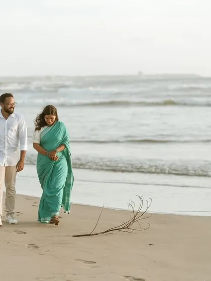 A full-length shot of the couple walking on the sand, capturing their relaxed interaction and the natural beauty of the coastal landscape.