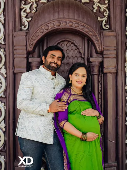 A happy couple portrait against a carved wooden door, showcasing a beautiful green and purple saree.