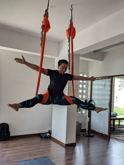 A student finds freedom and flight during an aerial yoga class, performing a perfect split with arms outstretched.