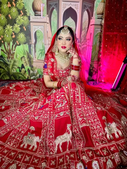 A beautiful bride seated against a vibrant backdrop. The makeup features a classic red lip and defined eyes, a look that is always in demand for traditional Indian weddings.