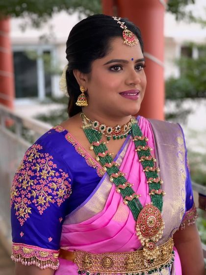 A portrait of Nirmala looking radiant for the ceremony. The makeup features a bold lip and defined eyes, complementing her pink and blue silk saree.